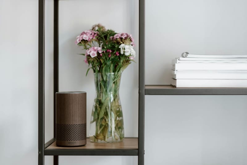 Elegant shelf setup with a smart speaker, vase of flowers, and stacked books for a minimalist touch.