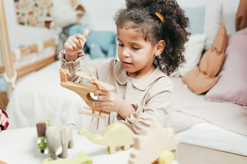 Young girl with afro hair enjoys playing with wooden toys in a cozy indoor playroom.
